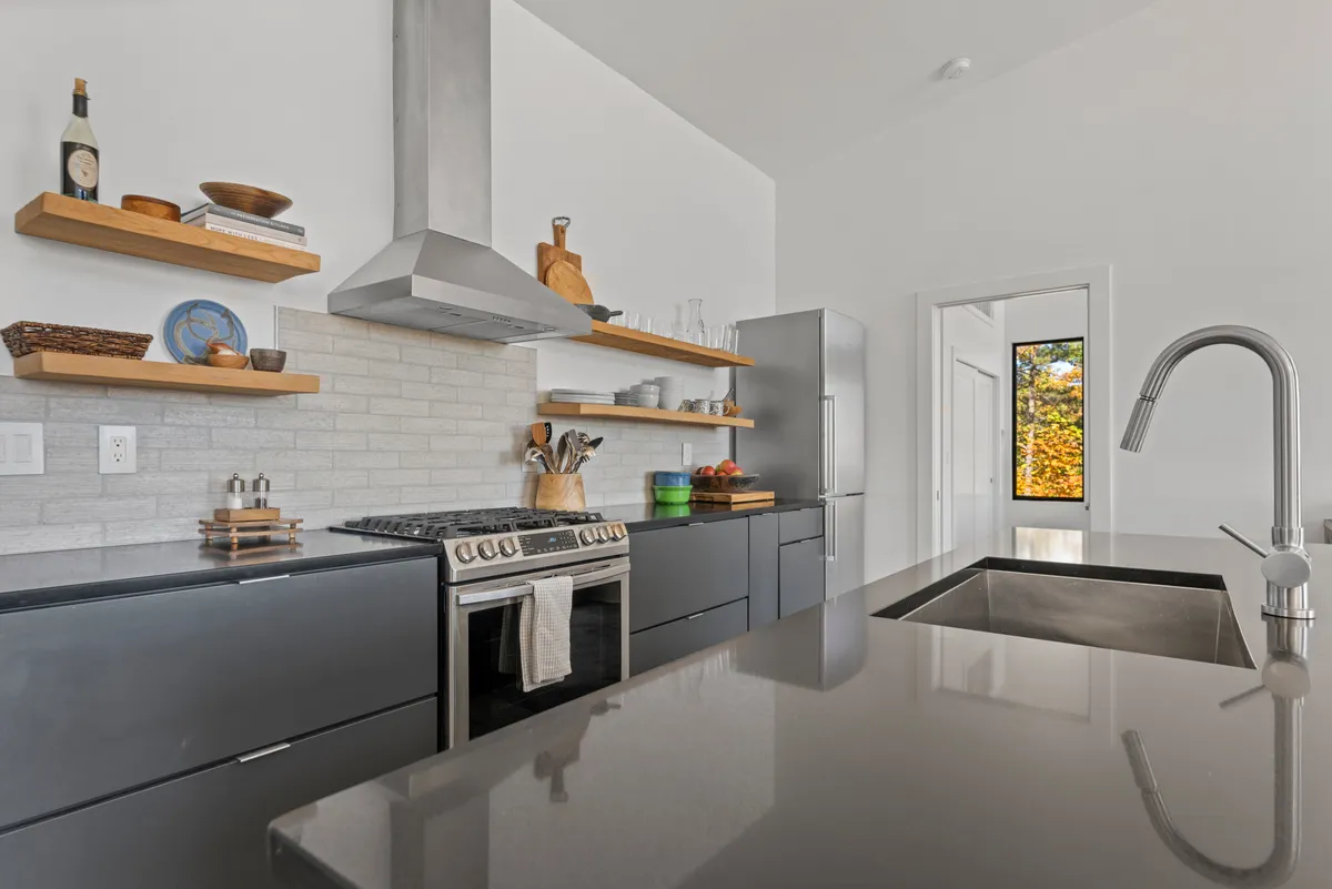 A functional and stylish kitchen environment featuring stainless steel appliances, open shelving with dishware, and an island with an integrated sink. The layout supports meal preparation, entertaining guests, and family gatherings, echoing a sense of warmth and practicality.