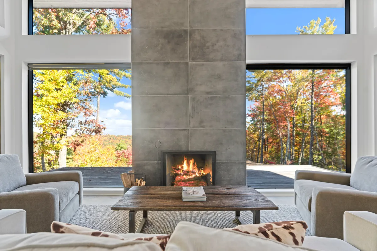 A warmly lit living space anchored by a central fireplace and large windows that look out to the natural surroundings. The coffee table and cozy seating create a welcoming atmosphere, ideal for gathering after outdoor activities or quietly watching the sunset.