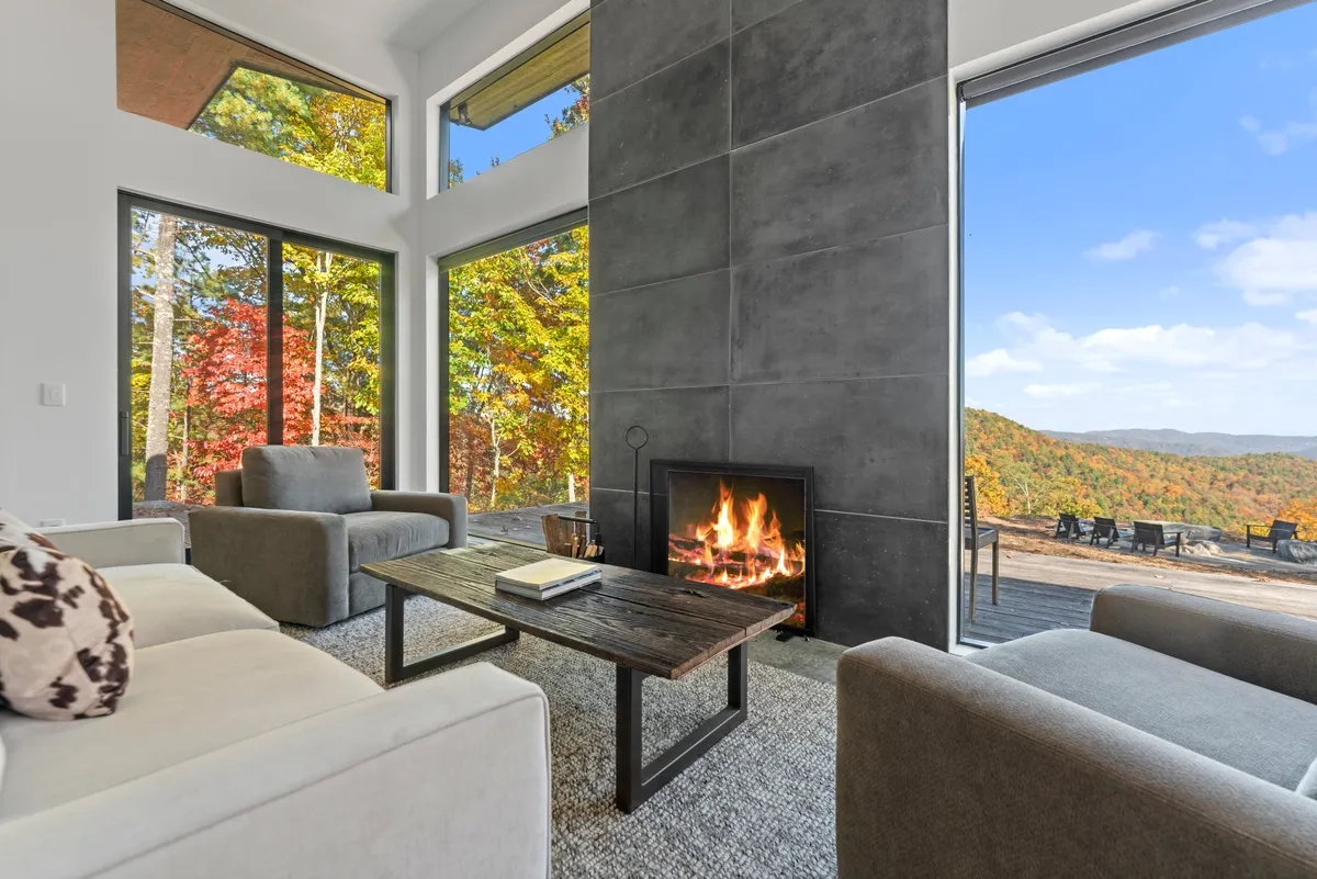 A warm, stylish great room featuring a crackling fireplace, large windows framing the landscape, a coffee table ready for board games, and comfortable seating perfect for relaxed conversation. The scene feels tranquil and inviting, ideal for indoor activities like reading or unplugged entertainment.