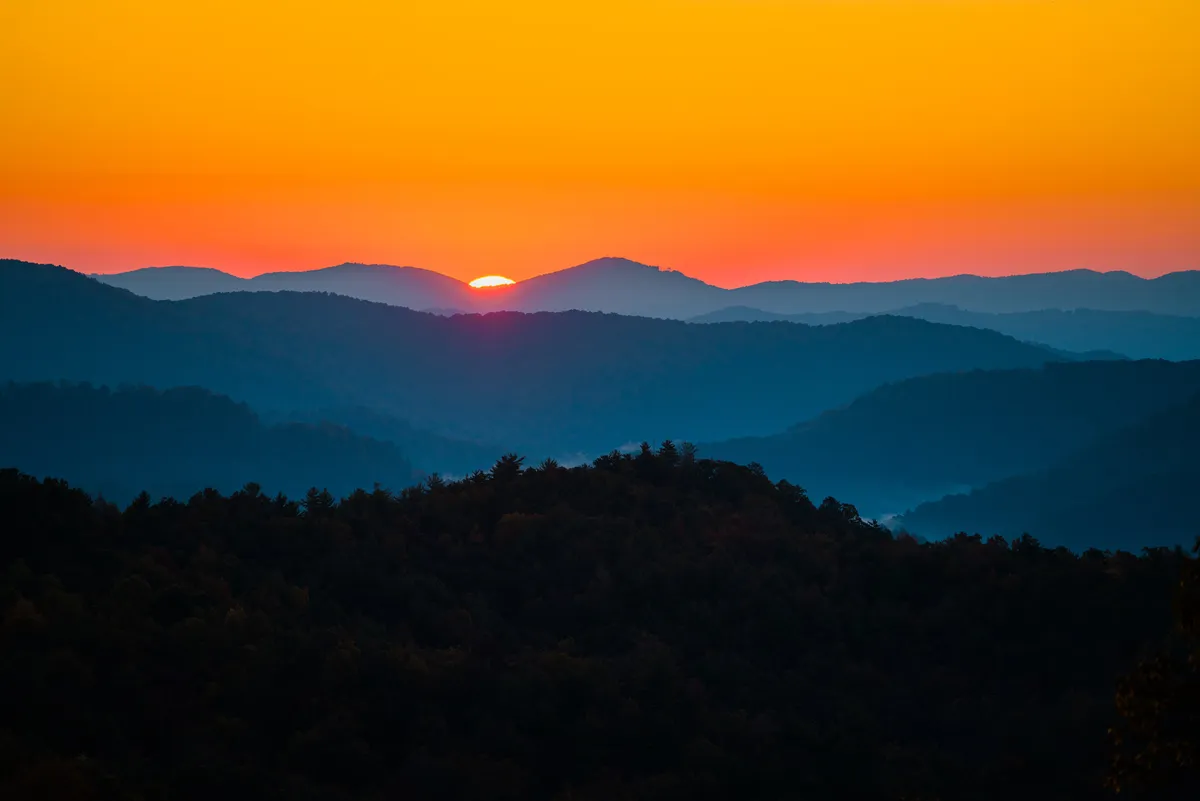 This image captures a breathtaking mountain sunset with silhouettes of distant peaks and a sky awash in soft gradients of color. The open landscape conveys a sense of adventure and natural beauty, inviting viewers to imagine themselves exploring the surrounding trails or unwinding after a day outdoors.