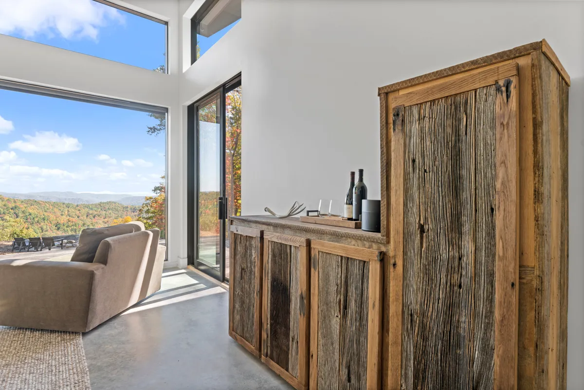 A serene interior view featuring a comfortable armchair, wooden cabinetry, and expansive windows offering a sunset view over the mountains. The cozy setup invites quiet reading, reflection, or conversation, reinforcing the idea of digital disconnection.