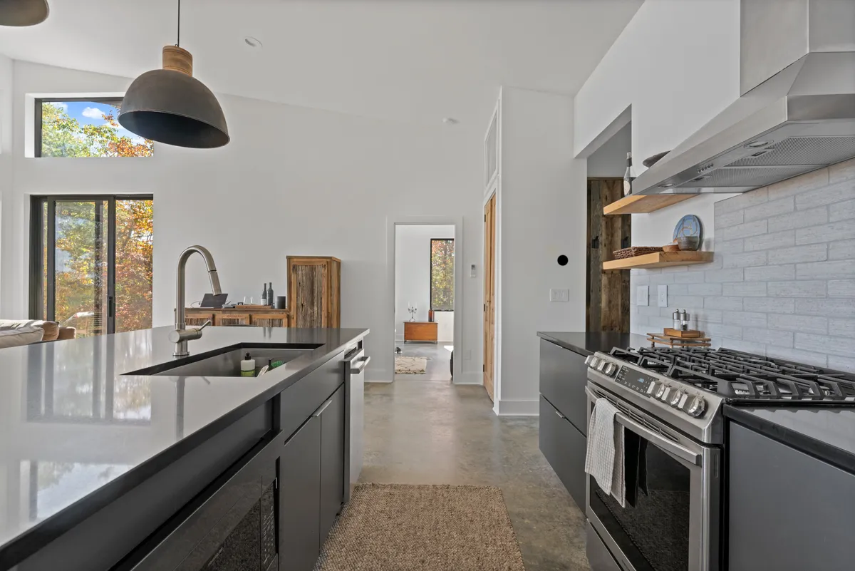An inviting kitchen with a central island surrounded by large windows, allowing natural light to flood the space. The stainless steel appliances add a touch of high-end European flair, while the island and seating create a welcoming spot for casual dining or shared culinary experiences.