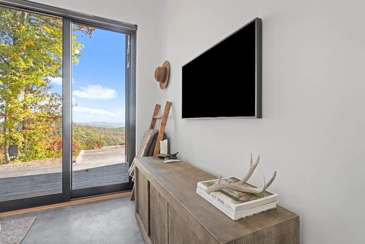 The scene features large glass doors opening to a sweeping outdoor view, with a wooden console table and decorative touches enhancing the inviting ambiance. The image creates a direct visual connection between indoor comfort and the vast natural landscape beyond.