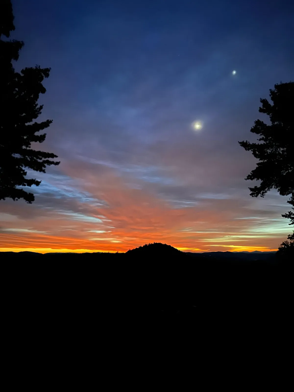 A stunning view of a vibrant sunset over distant hills, with silhouetted trees creating a dramatic yet calming scene. The open sky hints at the perfect conditions for stargazing and meditative reflection, echoing the section’s emphasis on natural beauty and private experiences.