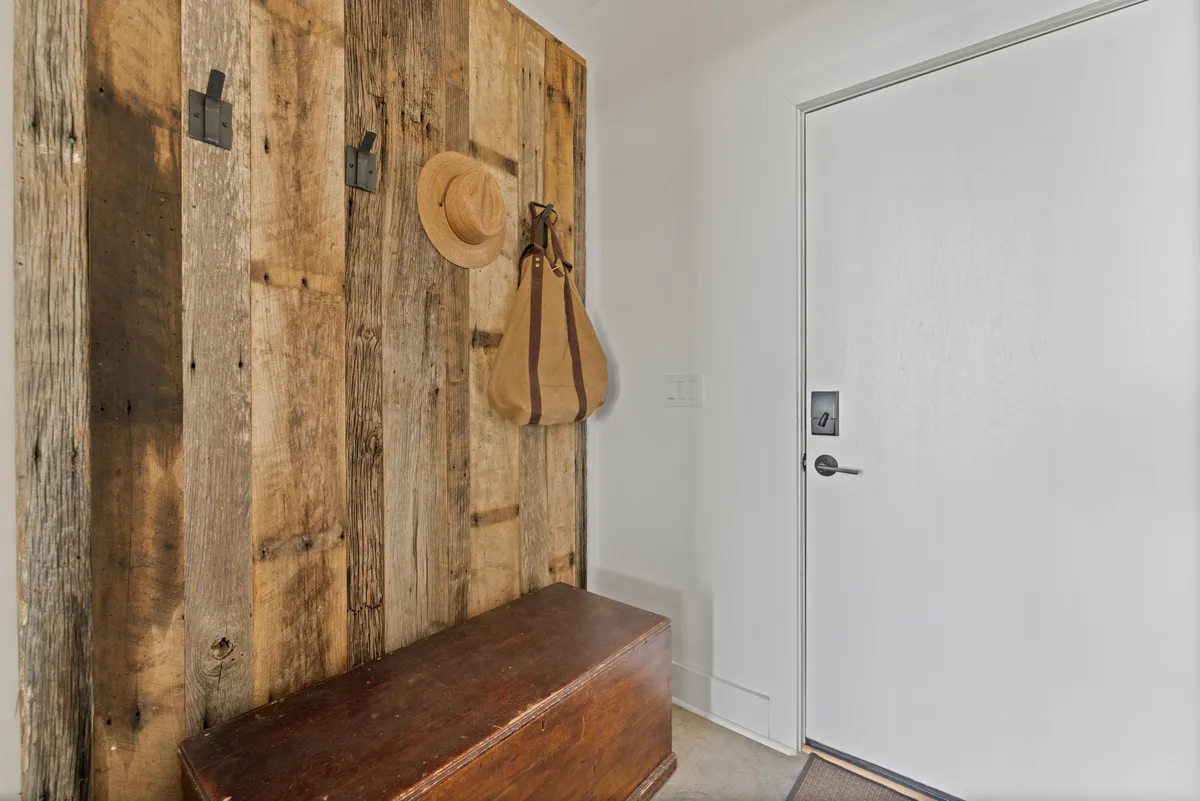 A cozy entryway with a wooden wall, bench, hat, and bag, suggesting a welcoming space for gearing up before heading out or unwinding after a day on the trails. The simple, functional design hints at the routines of adventure—preparing for hikes or returning home with muddy boots.